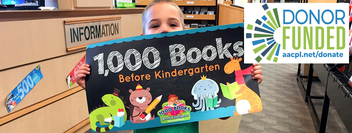 Young patron holding 1,000 Books Before Kindergarten graphic sign in library