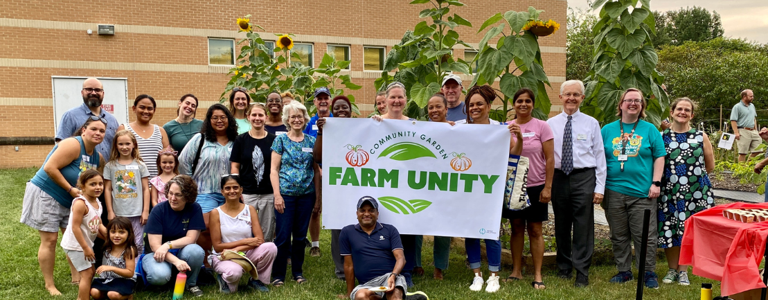 FarmUnity Harvest Fest 2023. A group of people holding a Farm Unity sign in front of the Community Garden at Crofton Library.