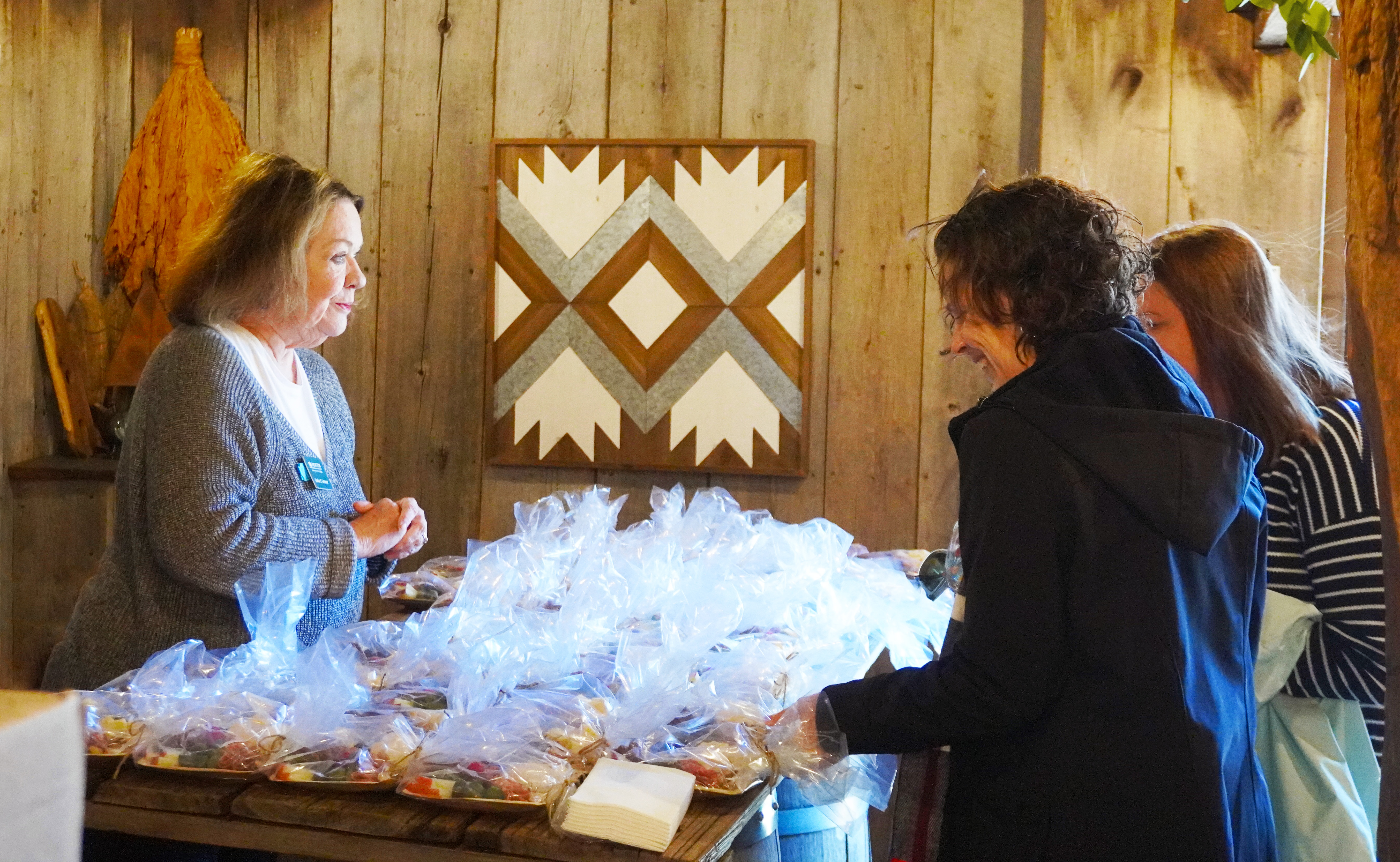 One person standing behind a table with charcuterie helping two people on the opposite side of the table.