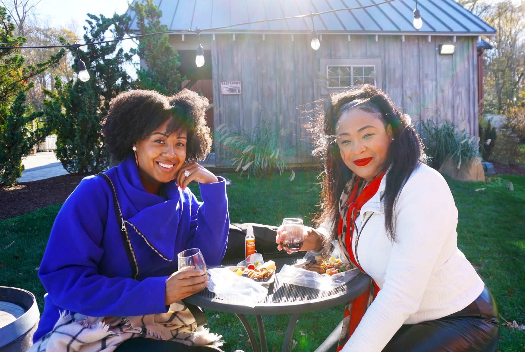 Two smiling women sitting outdoors while holding wine glasses.