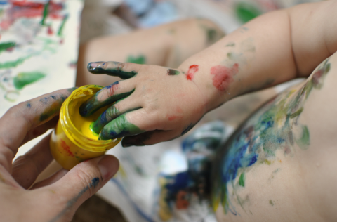 Photograph of a baby dipping their fingers into a paint pot.