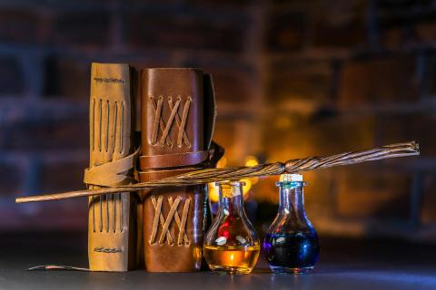 Table holding two leather books, a wooden magic wand, and two potion bottles holding yellow and blue liquid.