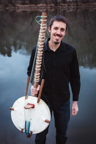 Man holding kora harp by a a body of water