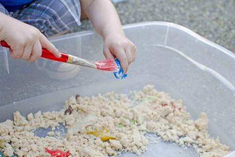 small child brushes away sand from a toy dinosaur