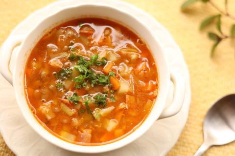 A warm bowl of minestrone soup and a spoon to the right.