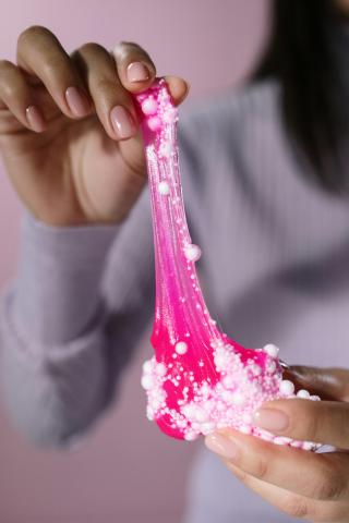 An image of a woman playing with pink slime filled with white foam beads.