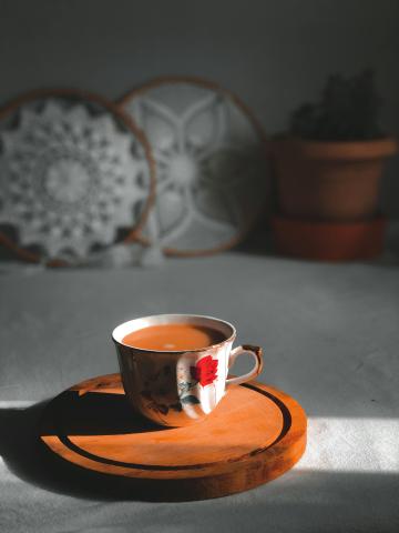 An image of a cup of tea resting on a wooden coaster. There are several plates in the background. 