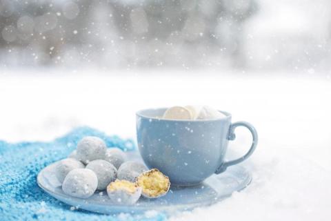 Light blue mug sitting on a plate holding truffles with a snowy background.