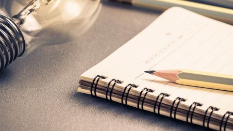 A pencil resting on a notebook next to a lightbulb