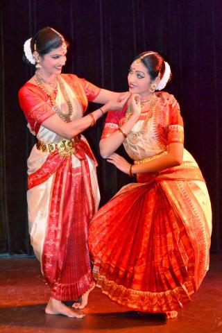 Two female dancers dressed in traditional Indian garments looking at one another.