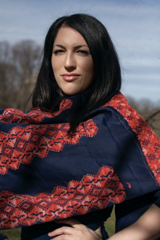 Portrait of Wafa Ghnaim wearing a Tatreez scarf of red embroidery on a blue fabric, photo credit Carlos Khalil Guzman, 2020