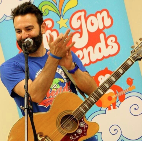 male with dark hair wearing a guitar and clapping in front of a microphone