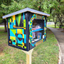 Chesapeake Arts Center Art Exchange Box at CRO is painted black with various shapes painted green, yellow, and blue